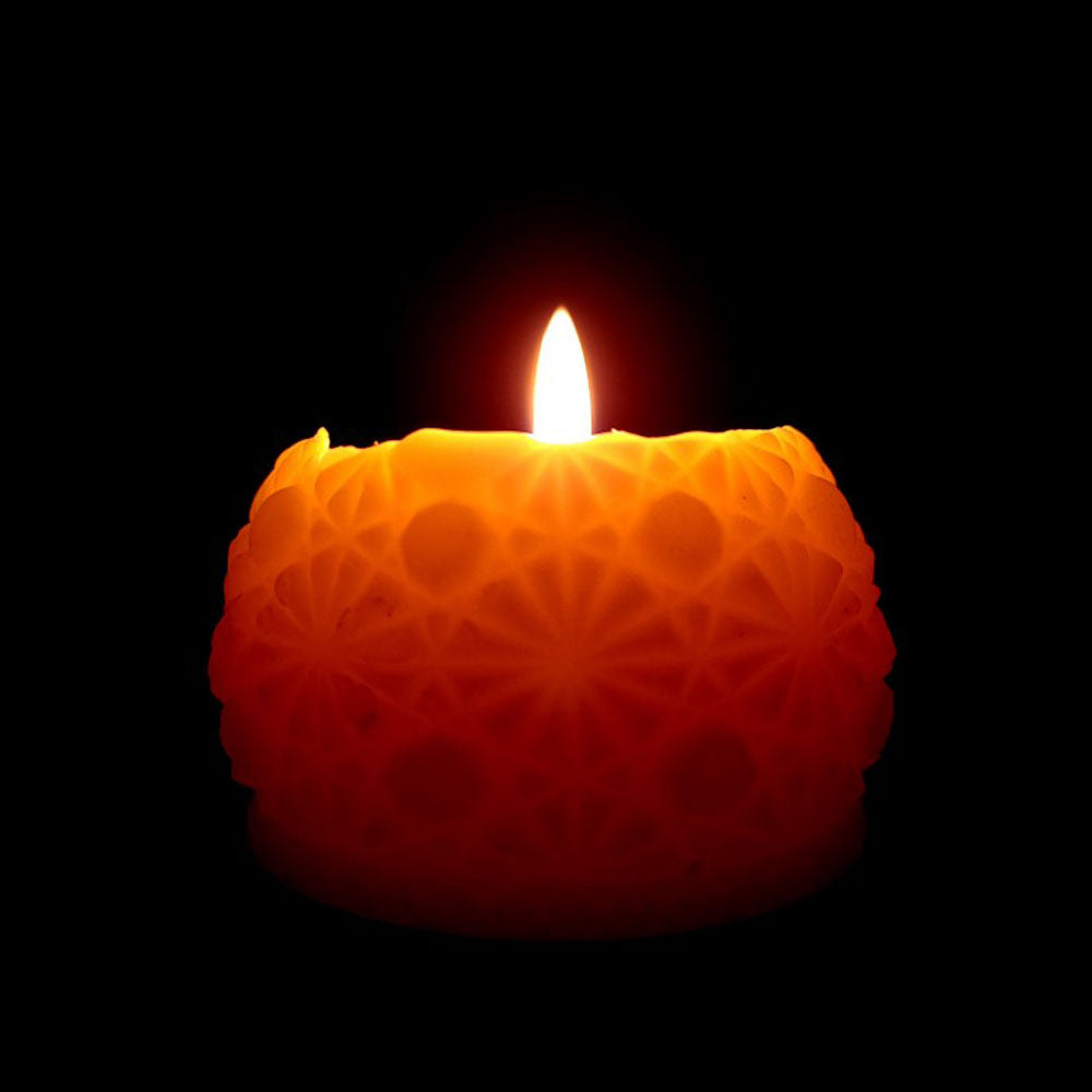 round beeswax candle with intricate pattern glowing as it burns