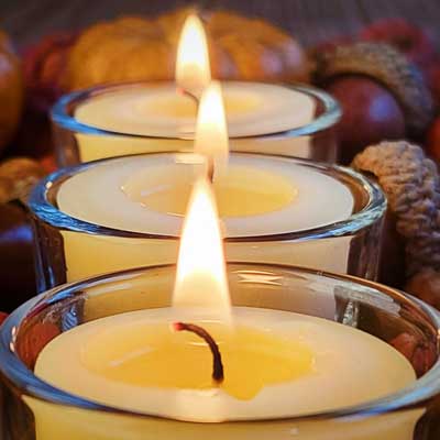 Close-up of three lit beeswax tealights in glass holders, each wick gently curved with a steady even flame above a melt pool.
