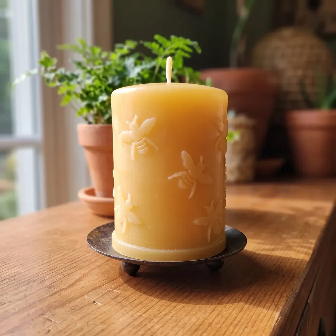 'Busy Bees' pure beeswax pillar candle with raised honeybee design, unlit on a footed metal dish in a sunlit garden room