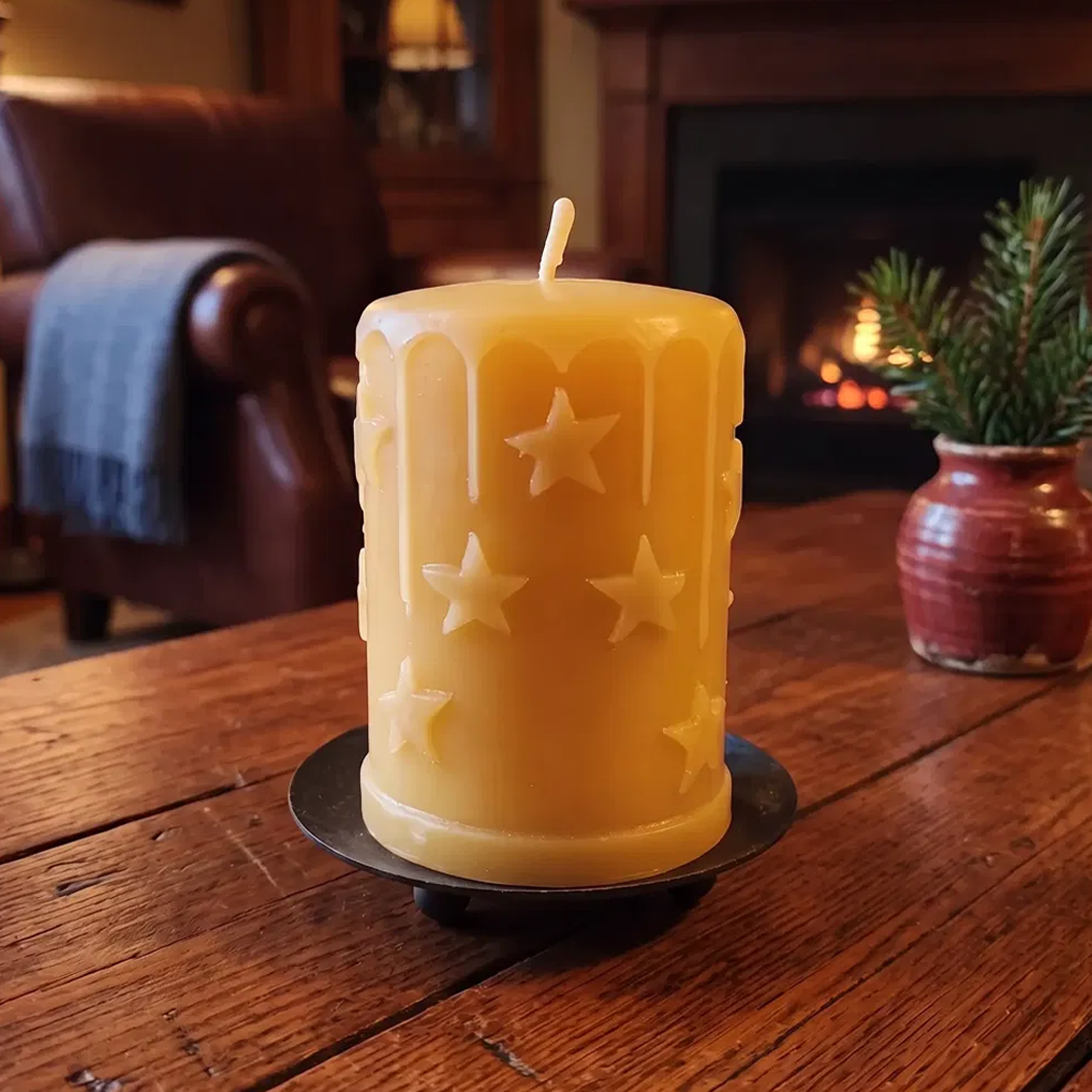 'Starry Starry Night' pure beeswax pillar candle with raised star design, on an iron plate in a warm fireside living room
