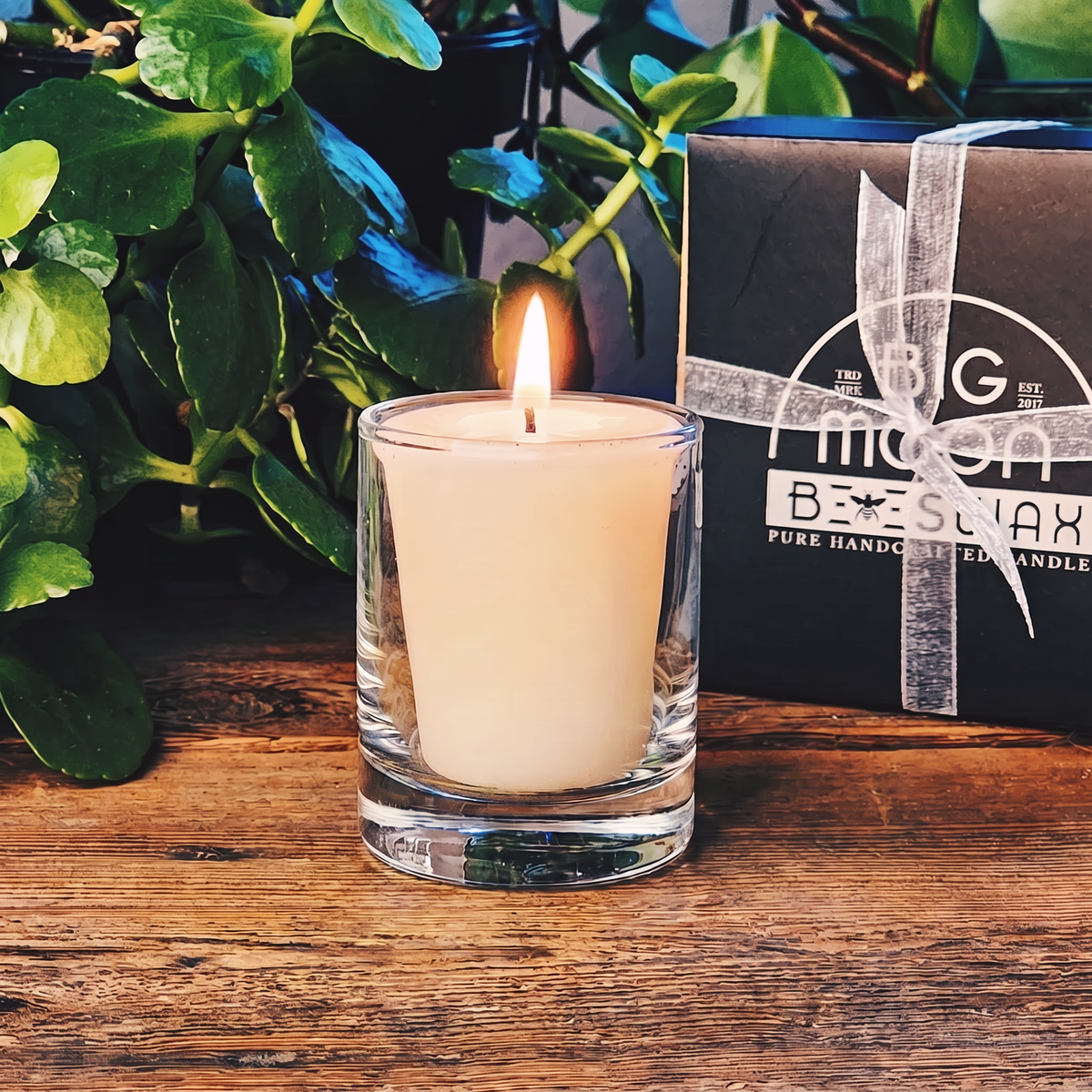 Silver Linings gift set: a lit ivory beeswax votive in a glass votive holder beside the ribboned Big Moon Beeswax gift box