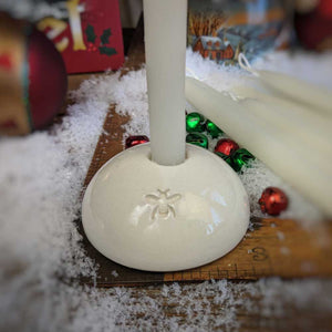 white ceramic taper holder with a bee stamped on it and an ivory tiny taper candle inside