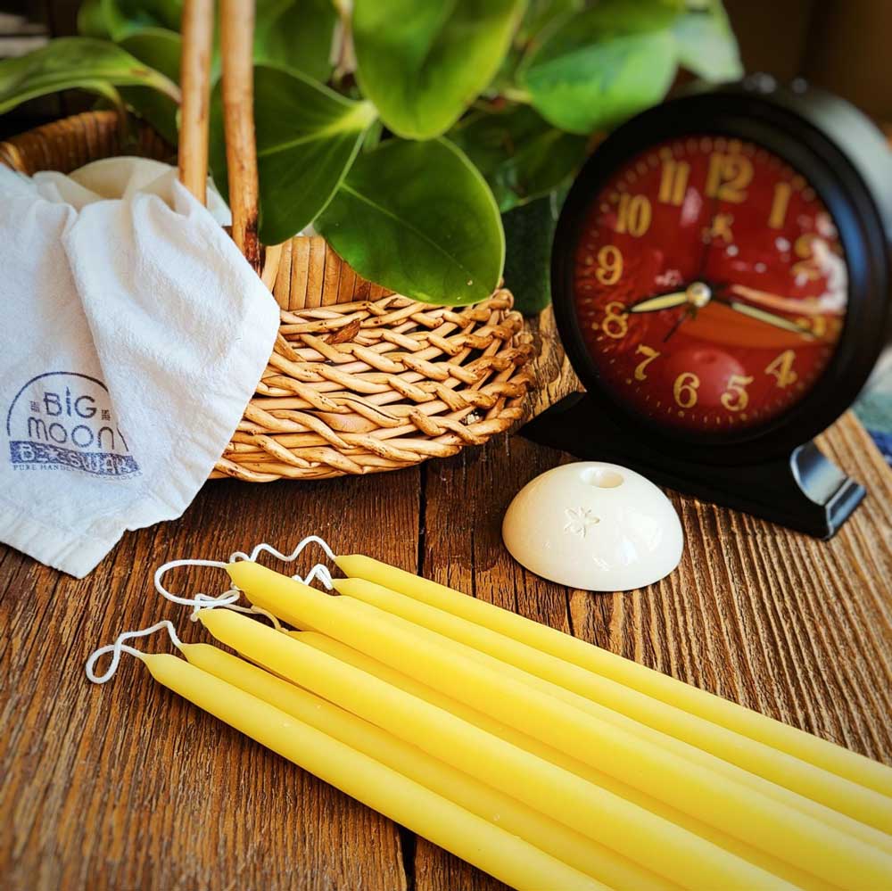 yellow tiny beeswax tapers lying on a table with a white ceramic taper holder next to them